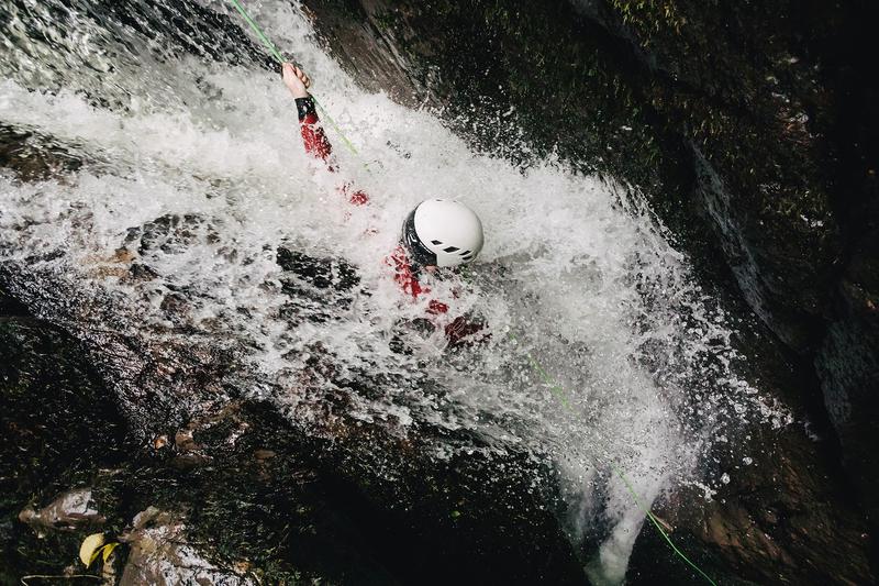 A person rappeling under the waterflow while canyoning.
